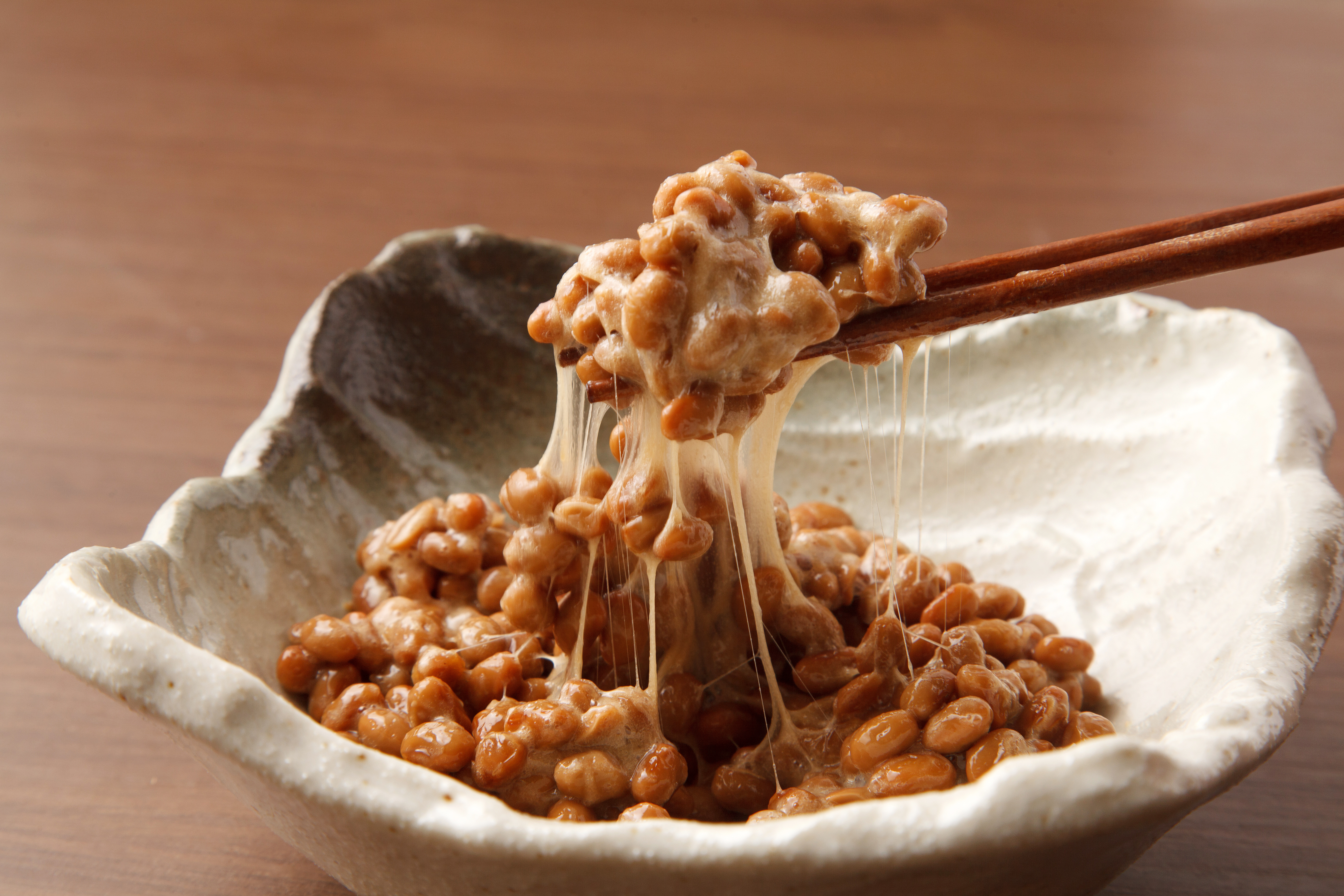 Traditional sticky natto lifted with chopsticks, showing its signature strands